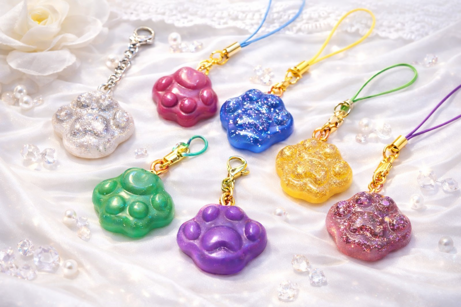 Porte-clés artisanaux en résine époxy faits main, en forme de patte, aux couleurs variées, disposés sur un tissu clair.