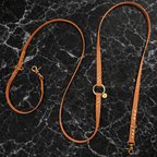 Laisse multiposition pour chien en BioThane marron, présentée dépliée sur un fond en marbre noir luxueux