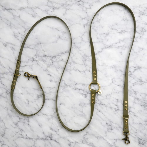 Laisse multiposition pour chien en BioThane olive, présentée dépliée sur un fond en marbre blanc luxueux